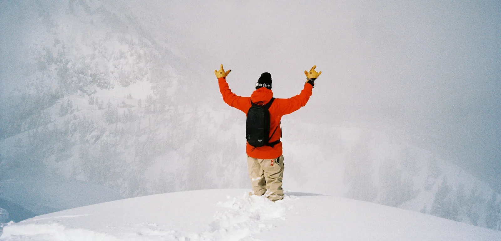 Snowboarder in a red 686 jacket with arms raised on a snowy mountain ridge