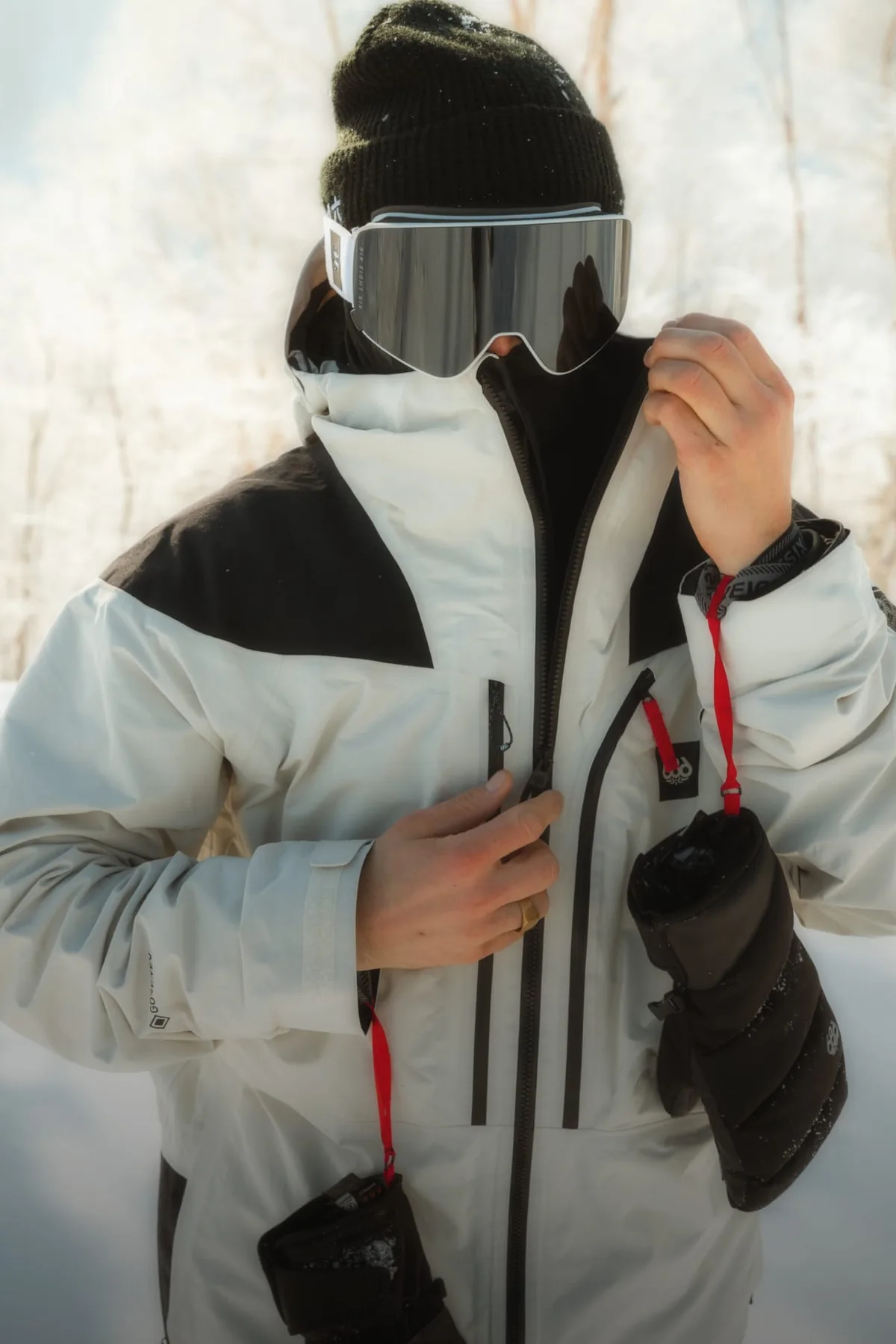Rider zipping a white and black 686 snow jacket with goggles pushed up on a beanie