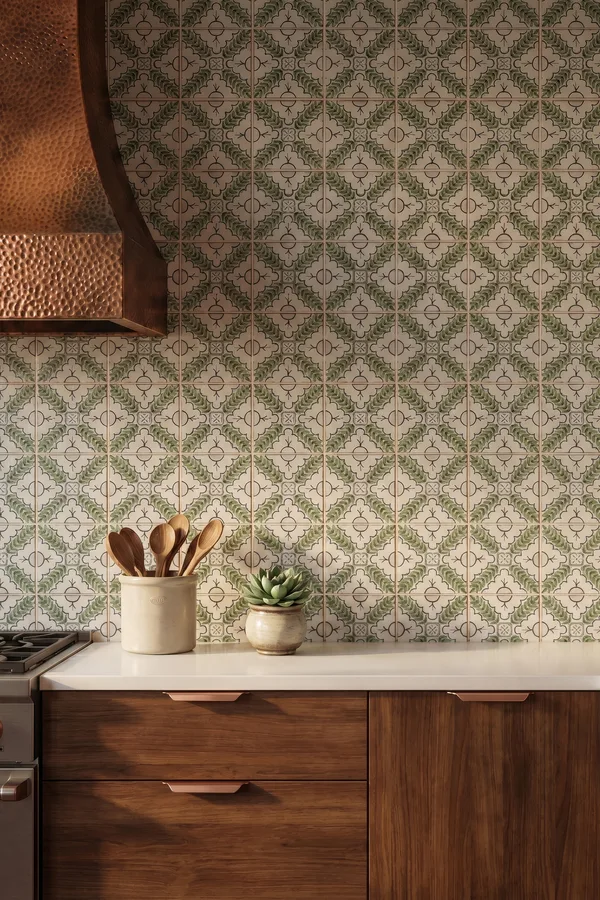 Kitchen backsplash in green and cream patterned Bedrosians tile beneath a copper range hood