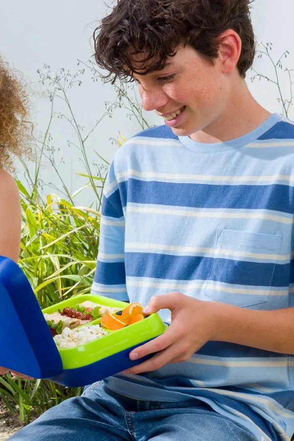 Teen opening a blue Bentgo lunch box outdoors