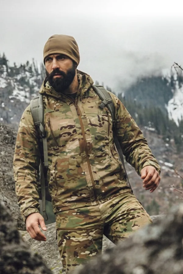 Hiker in a Beyond multicam jacket and beanie crossing rocky mountain terrain