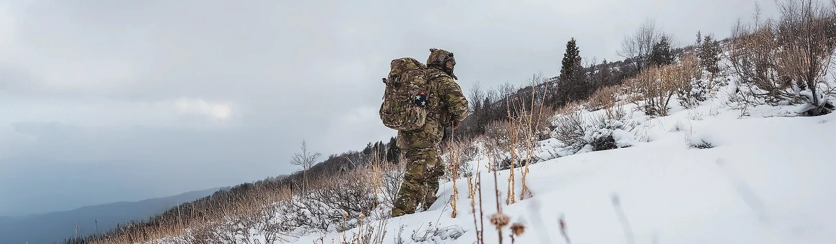 Soldier with a multicam pack climbing a snowy hillside in Beyond cold-weather layers