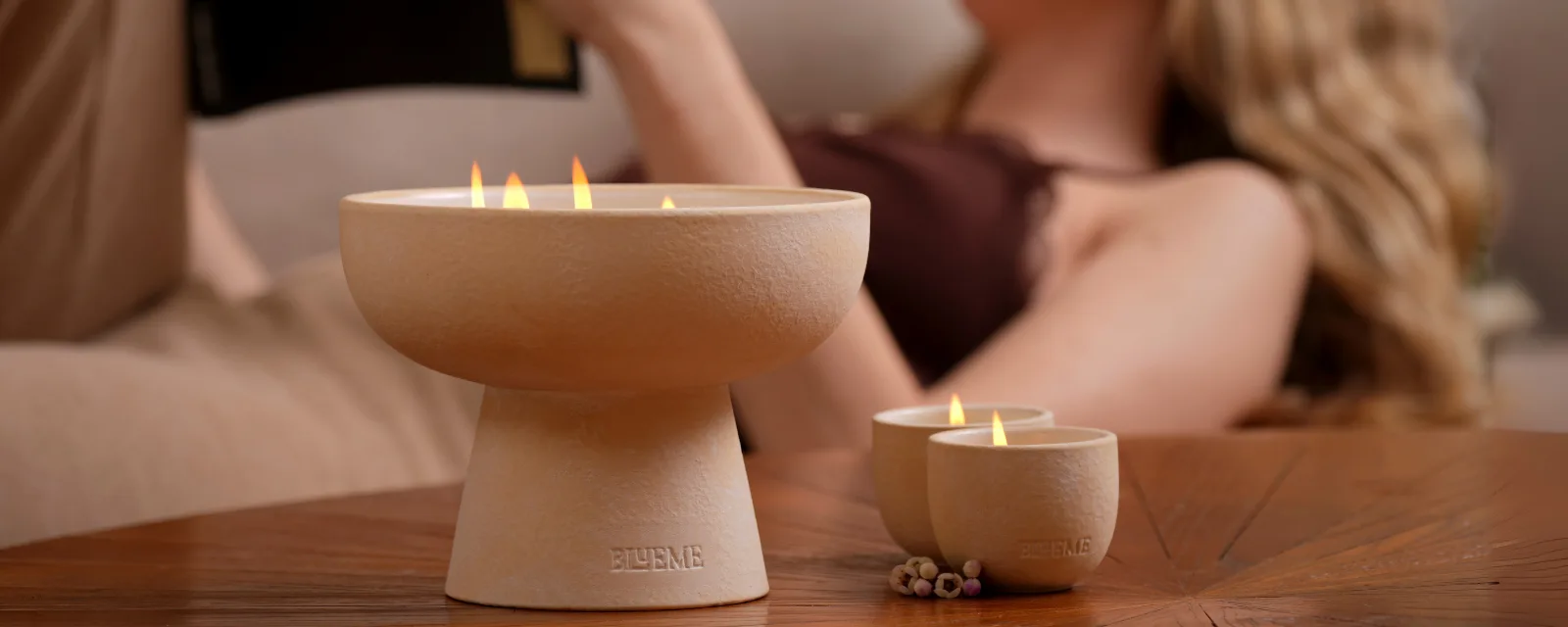 Blueme ceramic candles burning on a wood table with a woman relaxing behind