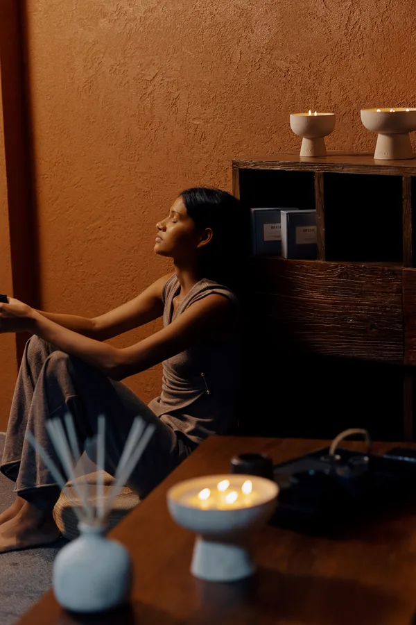 Woman resting beside lit Blueme ceramic candles and a reed diffuser