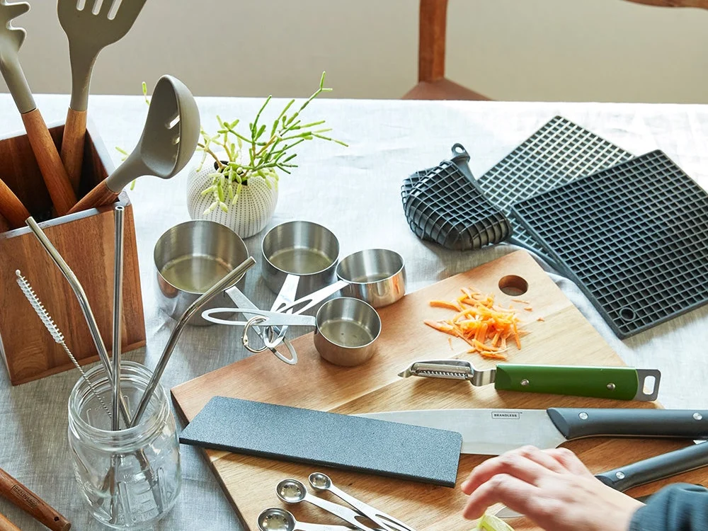 Brandless kitchen tools on a table: utensils, measuring cups, cutting board and chef's knife