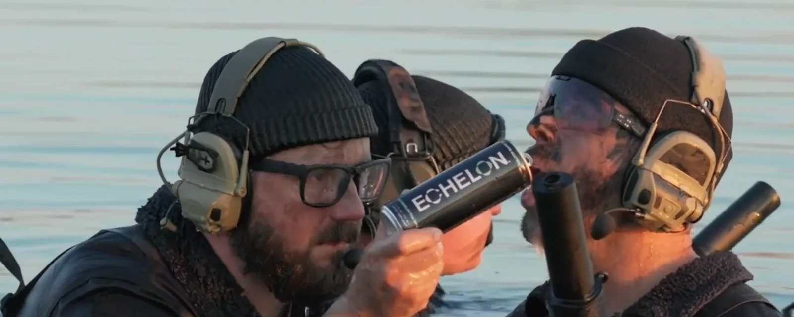 Men in tactical headsets in the water, one drinking from an Echelon can