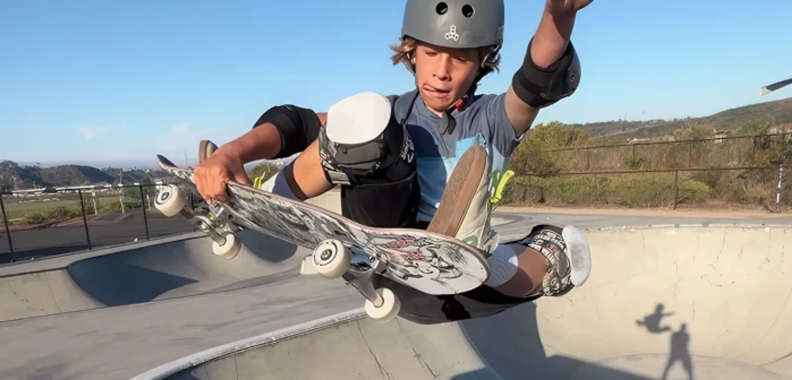 Young skater in a helmet and pads catching air above a concrete skate bowl