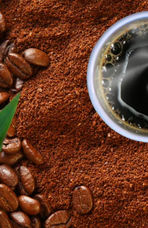 Close-up of coffee beans and grounds with a fresh brewed cup