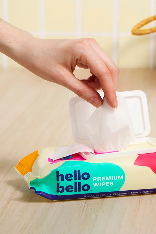 A hand pulling a wipe from a pack of Hello Bello Premium Wipes