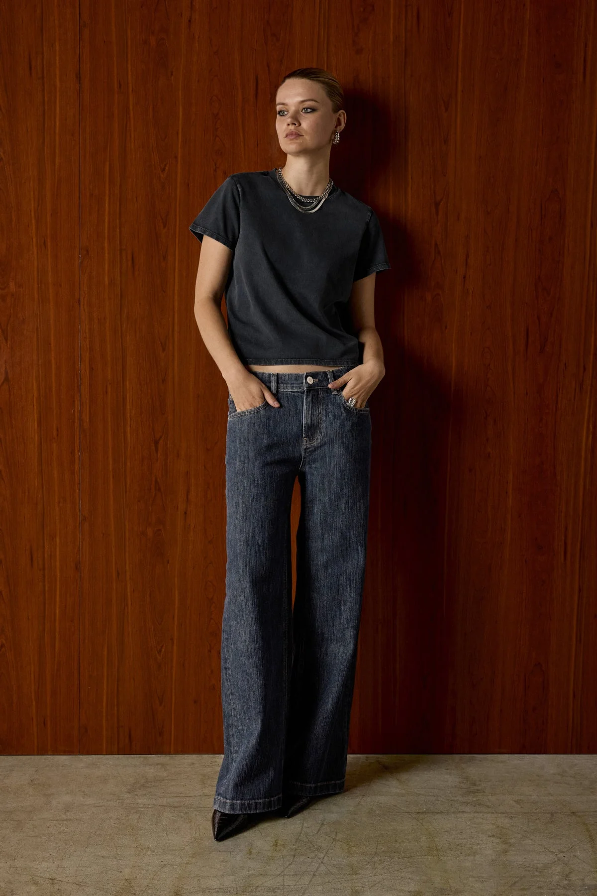 Model in a black tee and dark wide-leg Hudson jeans against a wood-panel wall