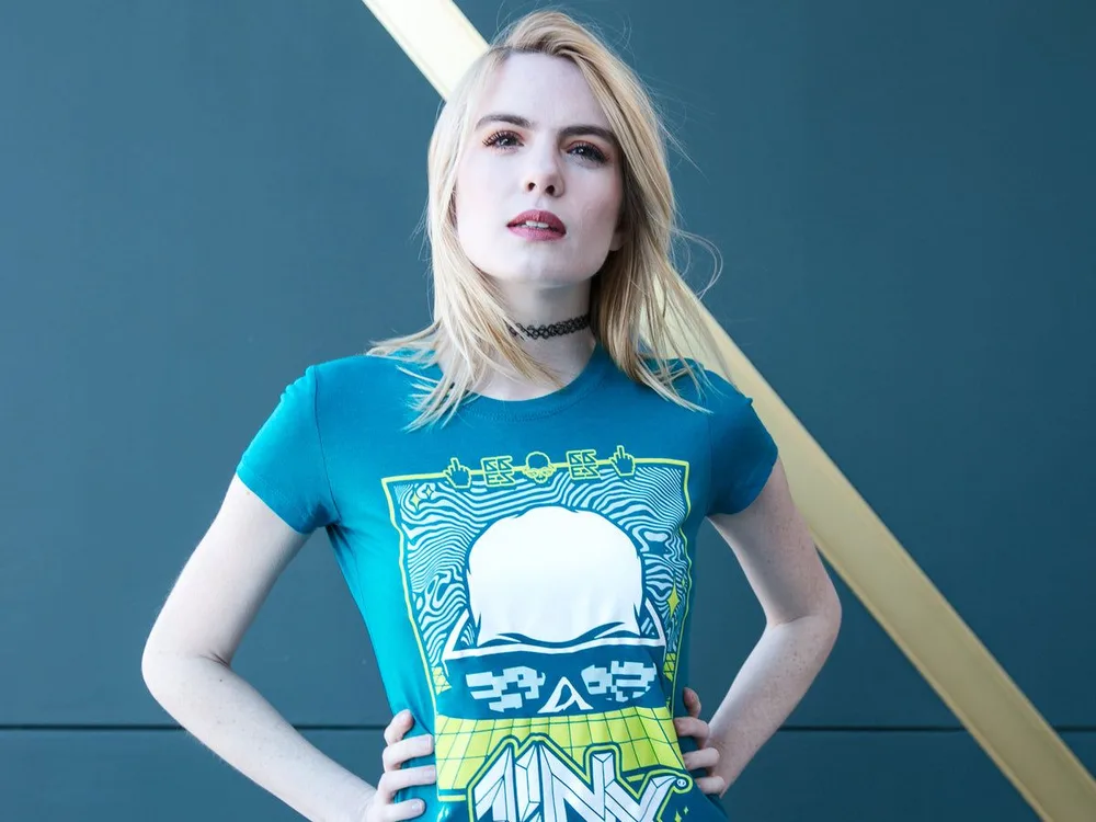 Model in a teal J!NX Get Rekt graphic tee against a blue wall