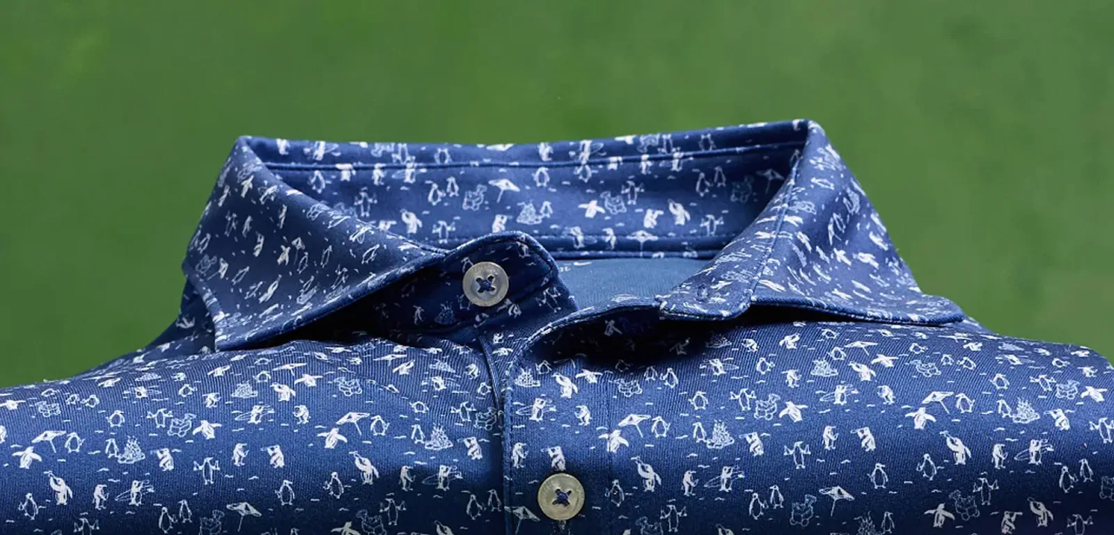 Close-up of a johnnie-O navy polo shirt with a white penguin print against green grass