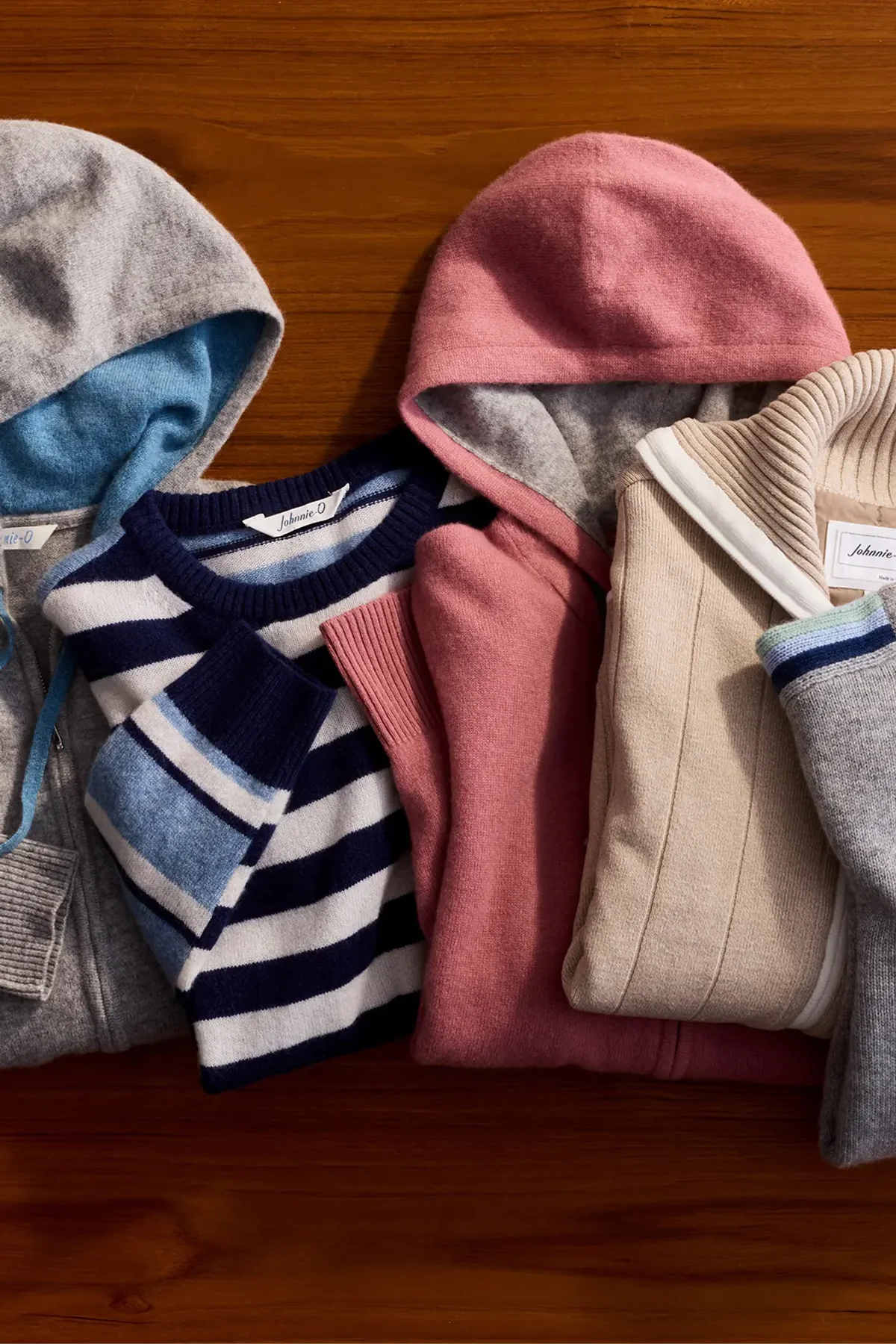 johnnie-O hoodies in grey, pink, cream and navy stripe laid out on a wood floor