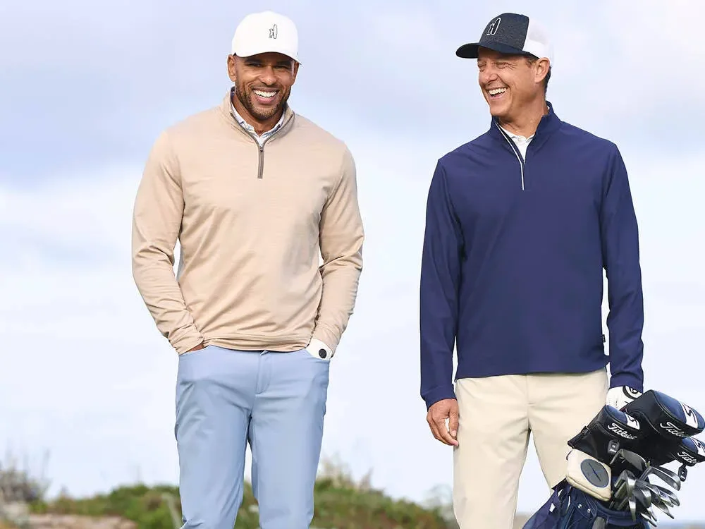 Two golfers laughing on a course in johnnie-O quarter-zips, one in tan and one in navy
