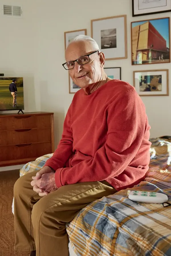 An older man sitting on his bed beside his TV and JubileeTV remote