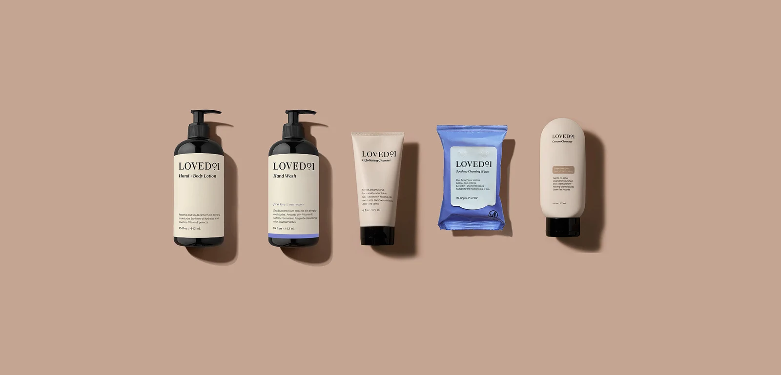 Five Loved01 body care products, including lotion and wash bottles, lined up on a tan backdrop