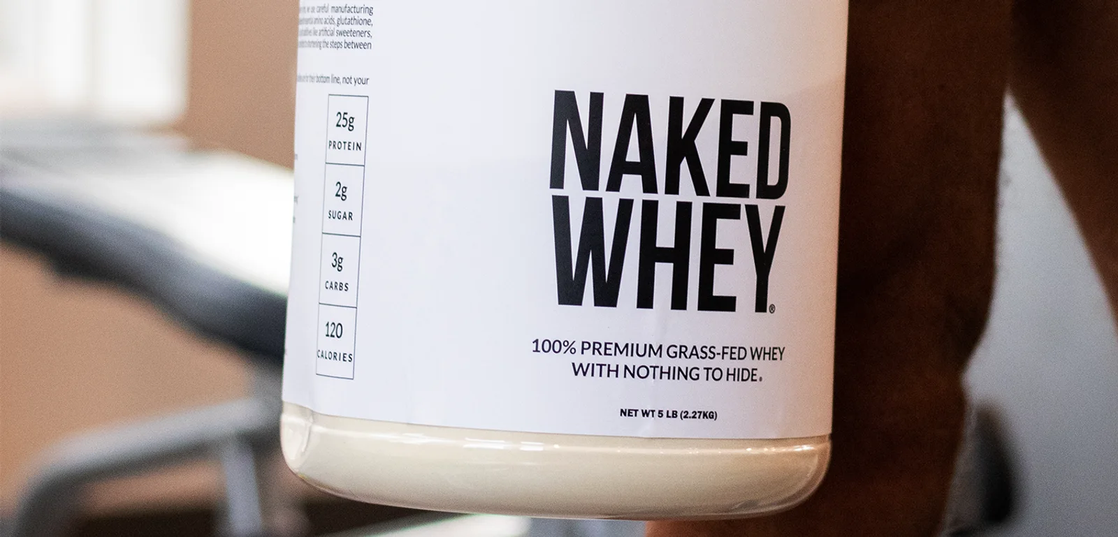 Close-up of a Naked Whey protein tub showing 25g protein and grass-fed whey label