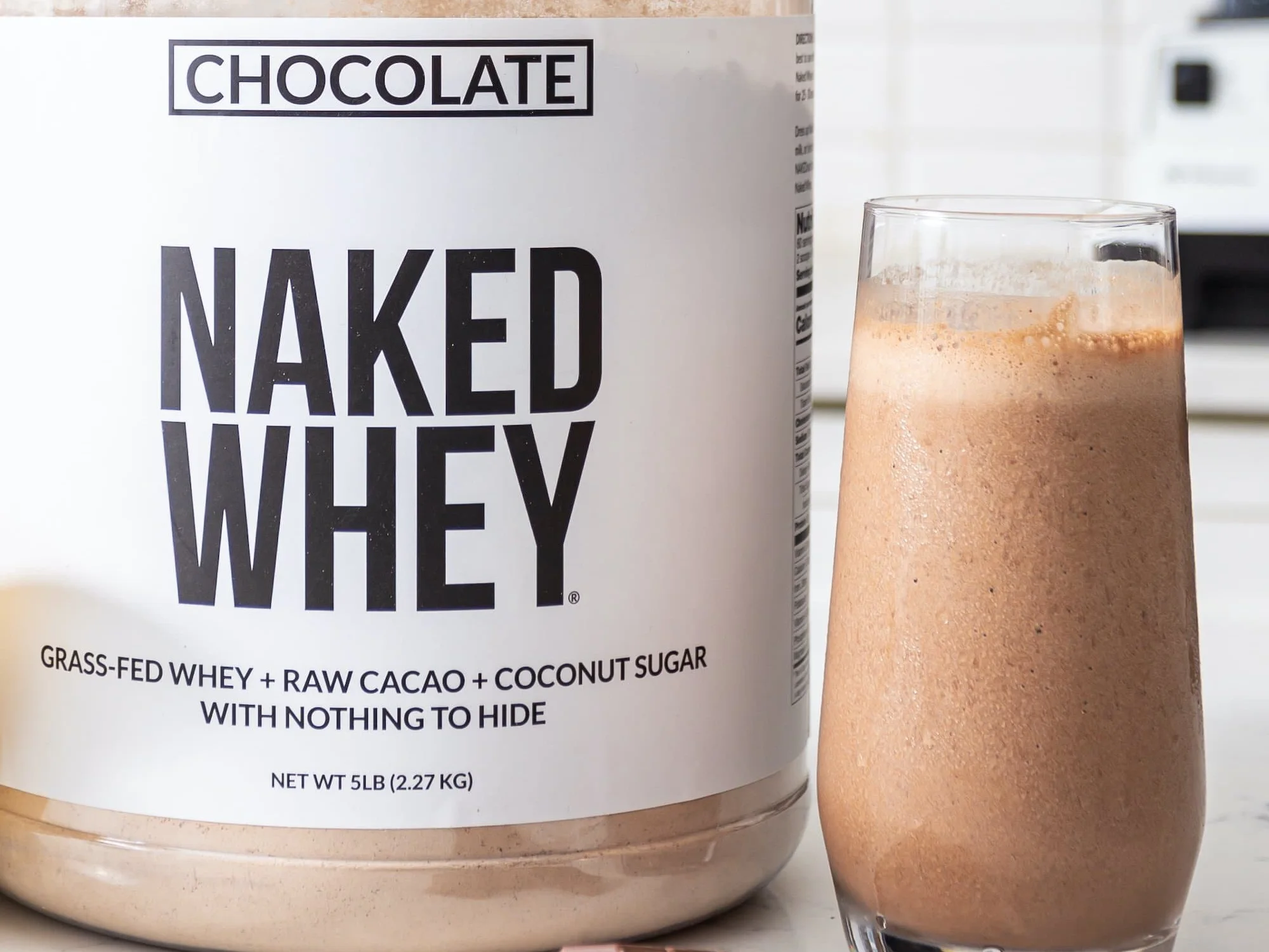 Tub of chocolate Naked Whey next to a glass of chocolate protein shake