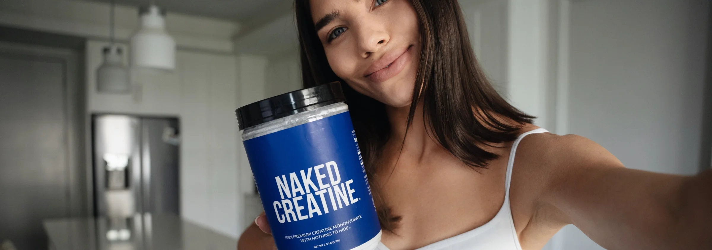 Woman holding a tub of Naked Creatine in a kitchen