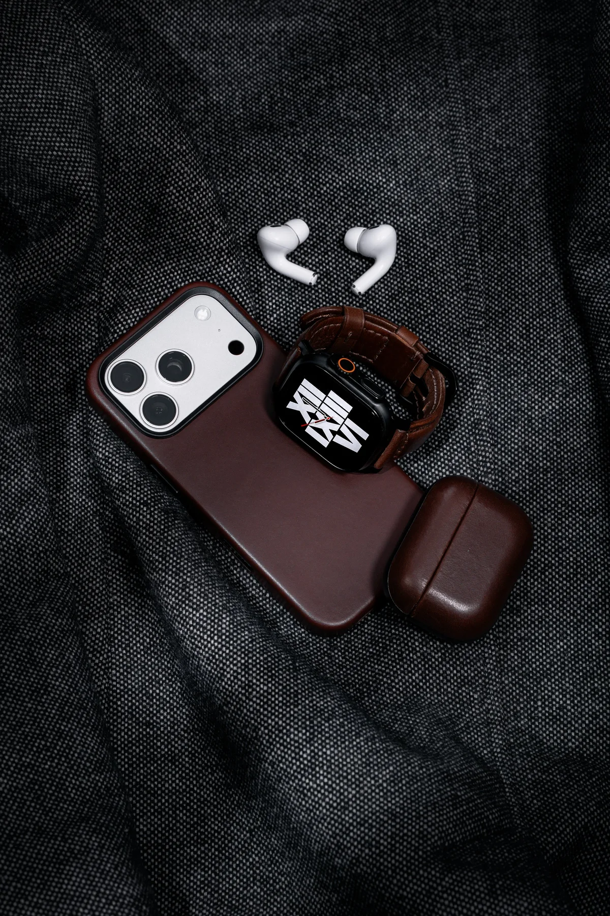 Nomad leather iPhone case, watch band and AirPods case on dark fabric