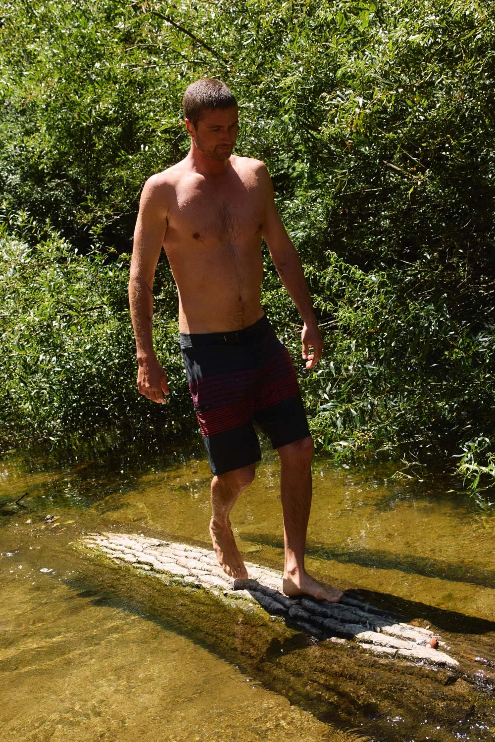Man in O'Neill boardshorts standing on a log in a creek