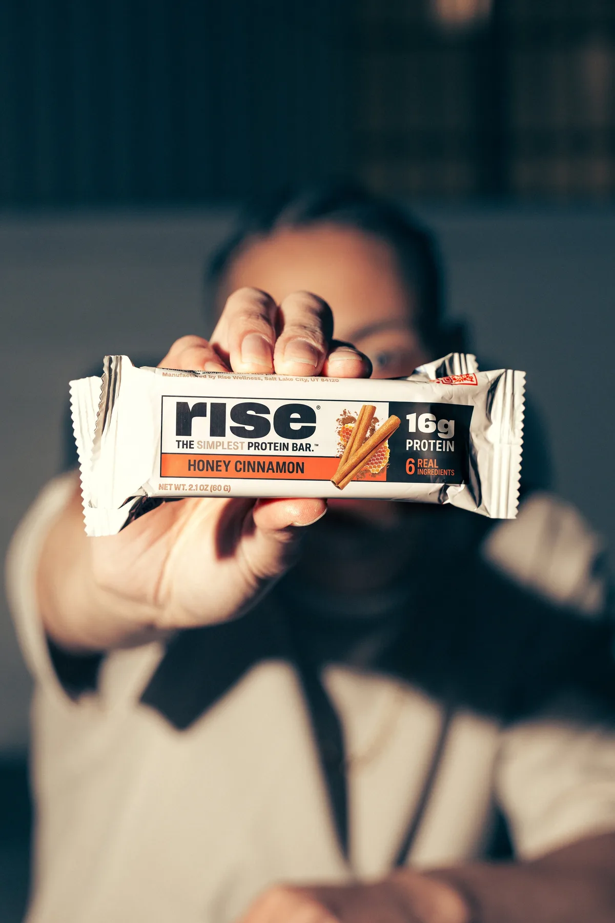 Person holding a Rise Bar Honey Cinnamon protein bar out toward the camera