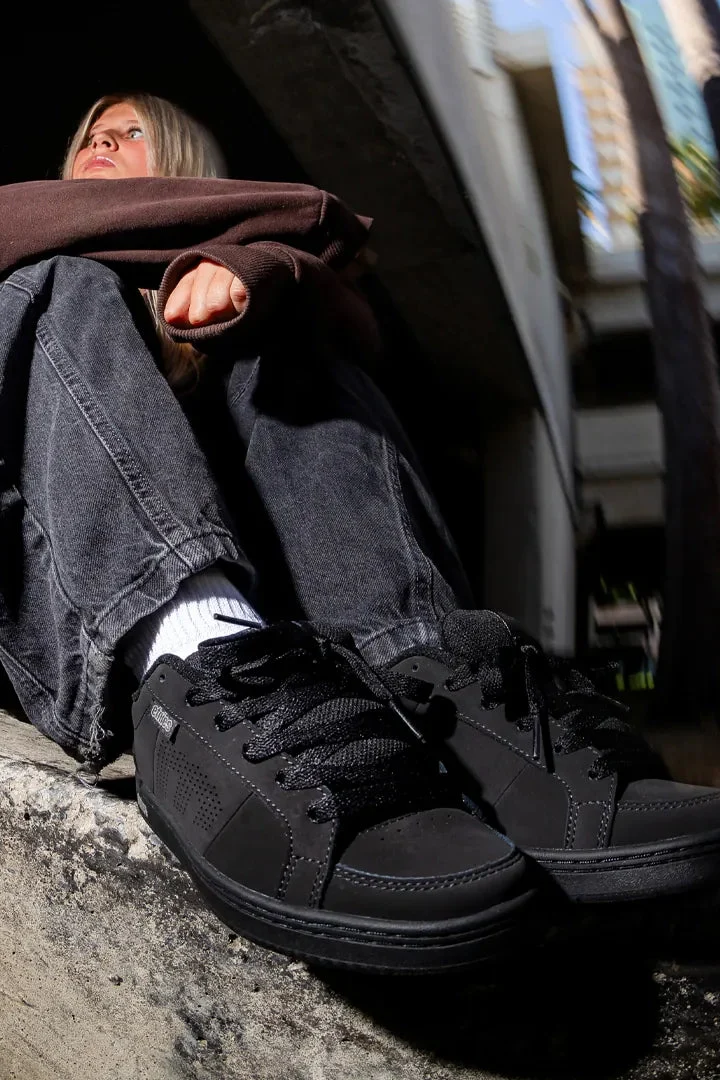 Skater sitting on a ledge wearing black etnies Kingpin skate shoes