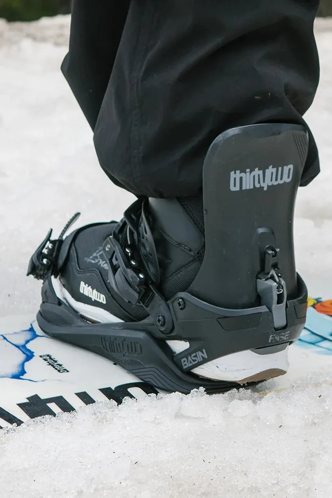 Rider stepping a thirtytwo snowboard boot into a binding on the snow