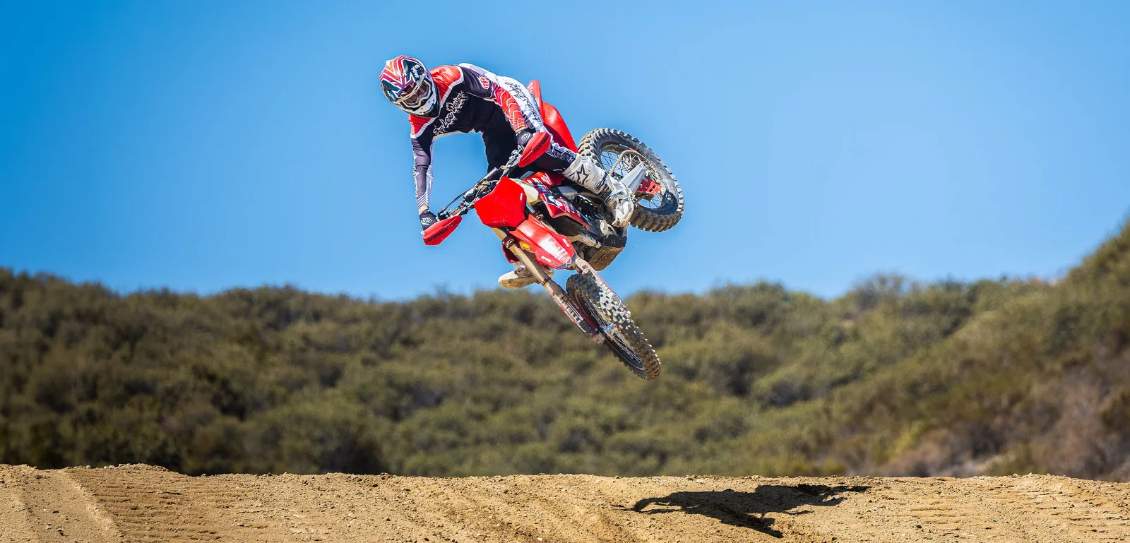 Troy Lee Designs motocross rider in red gear jumping a red dirt bike over a dirt track