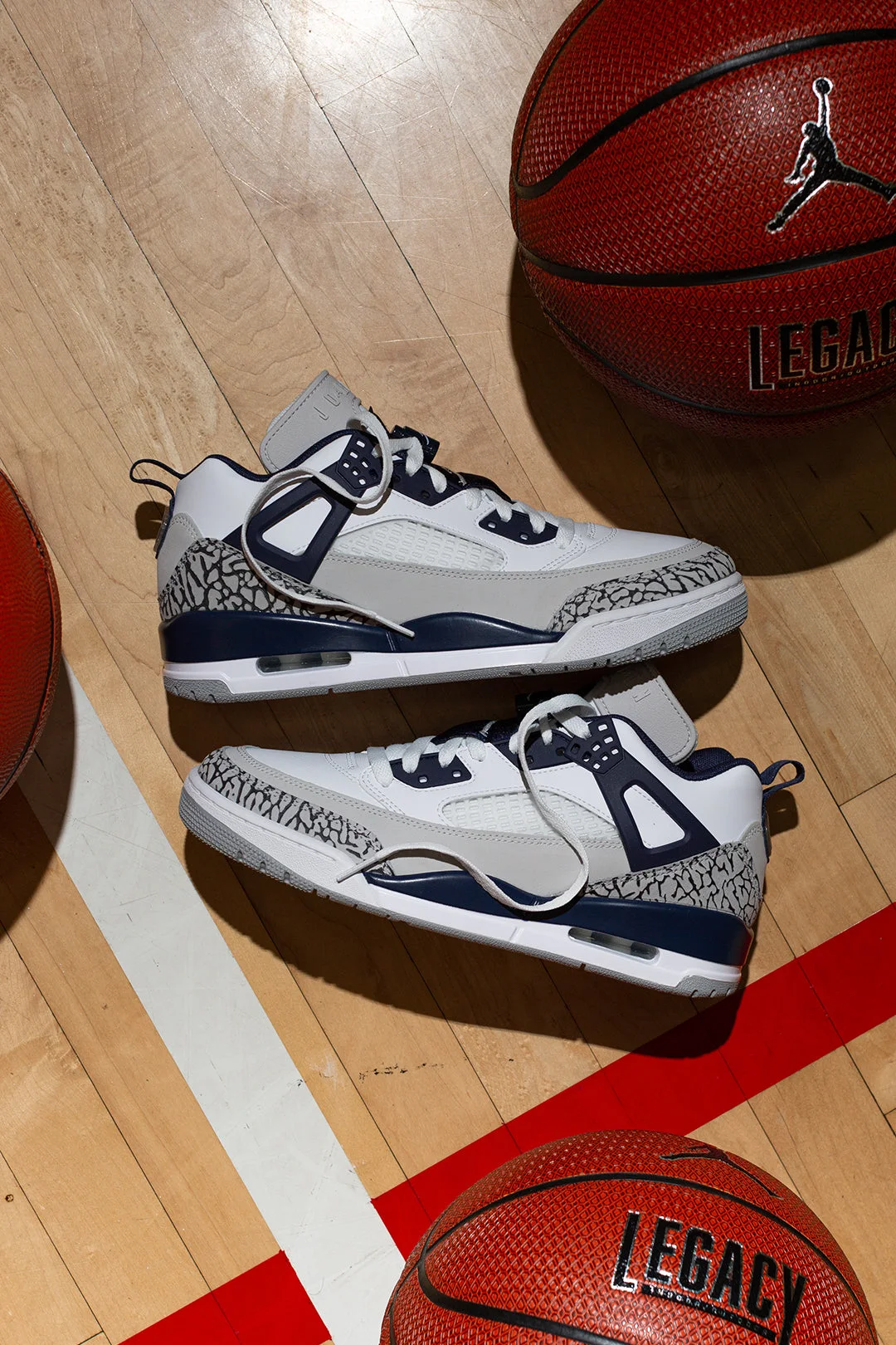 A pair of white and navy Jordan sneakers on a basketball court floor between two basketballs