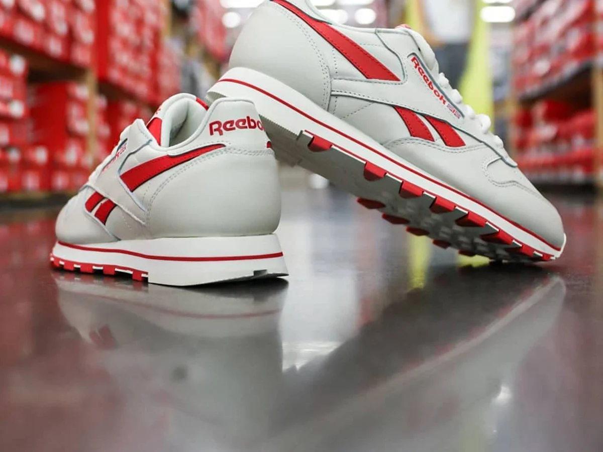 A white and red Reebok Classic leather sneaker in a shoe store aisle lined with red shoe boxes